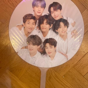 Stor bts fläkt - Denna produkt är en handfläkt med ett tryck av en BTS. Fläkten är rund med ett plastiskt handtag och motivet är i färg. Produkten är i gott skick utan synliga defekter. Perfekt för fans eller som samlarobjekt.