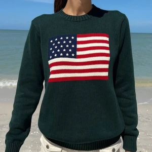 Mörkgrön stickad tröja med USA-flagga - Snygg mörkgrön stickad tröja från Brandy Melville med en stor amerikansk flagga på bröstet. Tröjan har rund halsringning och långa ärmar, perfekt för dig som vill sticka ut med en cool och klassisk look.                          67 cm length, 53 cm bust   100% cotton