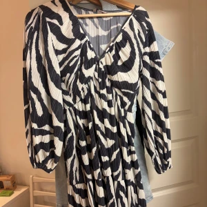 Zebramönstrad kortklänning från H&M - Säljer en plisserad kortklänning från H&M med svartvitt zebramönster. Klänningen har v-ringning. Väldigt bra skick, aldrig använd men inte prislapp kvar 