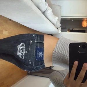 Victoria Beckham jeans med krona . Skinny - Mörkblå skinny jeans från Victoria Beckham med snygg krona i strass på bakfickan och blå patch med logga. Jeansen har låg midja och raka ben, skinny modell. klassisk femficksmodell och coola detaljer i silver. Perfekta för dig som vill sticka ut med lite extra bling.