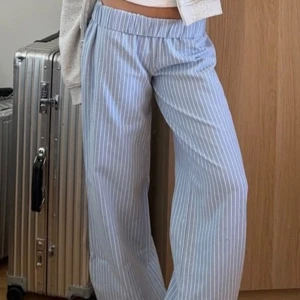 Randiga ljusblå byxor från Gina Tricot - Säljer ett par mjuka och sköna ljusblå byxor från Gina Tricot i storlek S. Byxorna har vita ränder, elastisk midja med snörning och ett loose fit med raka ben. Perfekta för chill dagar eller när du vill vara extra comfy.