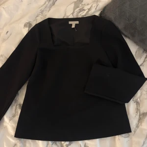 Svart långärmad blus från H&M - Stilren svart blus från H&M i storlek XS med fyrkantig halsringning och långa ärmar. Toppens enkla design gör den lätt att matcha med olika outfits. Materialet känns mjukt och har en lätt struktur, perfekt för dig som gillar minimalistisk stil. Endast andvänd 1 gång 