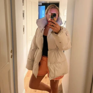 Beige pufferjacka från Meotine XS/S - Säljer en beige pufferjacka från Meotine i storlek XS/S. Jackan har hög krage, dragsko i midjan och knappar framtill. Oversized passform och långa ärmar. Perfekt för kalla dagar🤩