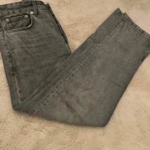 Grå jeans från 157, straight fit slitna nere - Säljer ett par grå jeans från 157 med rak passform och klassisk femficksdesign. Jeansen har en snygg tvättad look och råa, slitna kanter vid bensluten för en cool vibe. Perfekt för dig som gillar streetstyle och vill ha något som sticker ut.