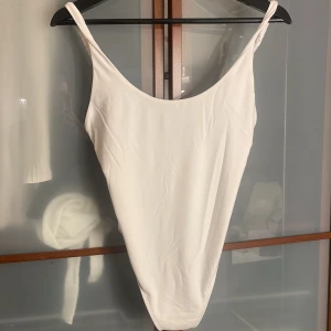 Vit body från Bershka, storlek M - Snygg vit body från Bershka i storlek M. Modellen har smala axelband med rynkade detaljer och djup rygg. Enkel och stilren design. Aldrig använts. 