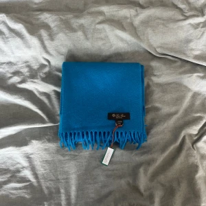 Blå kashmirhalsduk från Loro Piana - Supersnygg blå halsduk från Loro Piana i 100% kashmir. Den är mjuk, har klassiska fransar i kanterna och en stilren design utan mönster. Perfekt accessoar för att lyfta din outfit med en pop av färg och lyxig känsla. Helt ny med tags 
