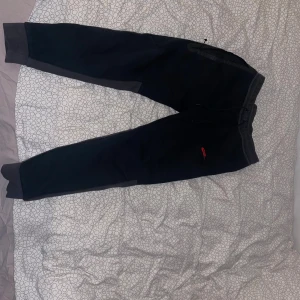 Svarta mjukisbyxor från Nike - Nike mjukisbyxor i svart med mörkgrå detaljer på benen och muddar vid fotleden. Byxorna har elastisk midja och röd Nike-logga på framsidan. Perfekta för chill eller träning, tillverkade i mjukt bomullsmaterial. Storlek L men passar mig som har M