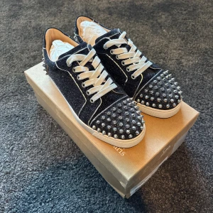 Christian Louboutin skor - Säljer ett par svarta glittriga sneakers från Christian Louboutin med vita snören och silverfärgade nitar på tå och häl. Skorna är i jättefint skick (9,5/10)! Alla tillbehör följer med!
