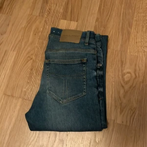 Blå jeansbyxor 29/32 - Säljer ett par klassiska blå jeansbyxor i storlek 29/32. Jeansen har fem fickor, normal passform och raka ben. Snygg tvätt med lätt slitning på låren och diskreta detaljer. Perfekta för dig som gillar en enkel och tidlös look.
