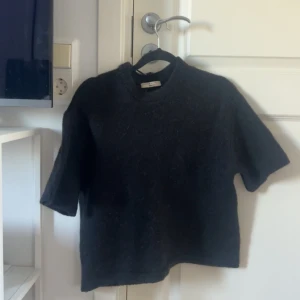 Svart stickad tröja från Gina Tricot - Svart stickad tröja från Gina Tricot i premiumkvalitet. Tröjan har korta ärmar och en klassisk rund halsringning. Perfekt för lager-på-lager och funkar året runt. Enkel och stilren design som passar till allt.