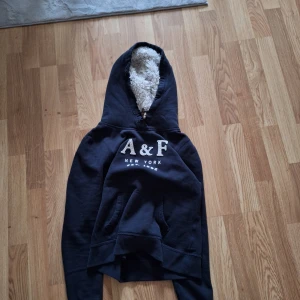 Mörkblå hoodie från Abercrombie & Fitch - Säljer en sjukt efterlängtad och sällsynt hoodie från Abercrombie & Fitch eftersom den inte passa mig. med broderad logga framtill och för skön inline fur i. Perfekt för kyliga dagar när du vill vara både bekväm och archive. Har av er vid fler frågor! Längd:56cm armar 66cm axlar 48cm