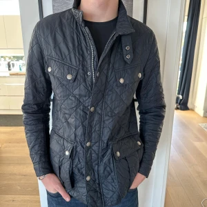 Svart quiltad jacka från Barbour - Quiltad svart jacka från Barbour med snygga tryckknappar och dragkedja framtill. Perfekt för dig som gillar stilren och klassisk look. Perfekt skick, inga defekter. Nypris 3200kr. Vårat pris 799kr. Modellen är 186 cm. Storlek L. Skriv vid minsta intresse!