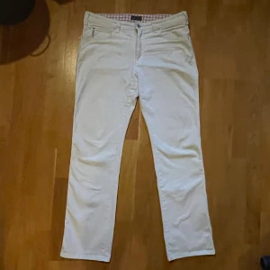 Vita byxor från Armani Jeans - Snygga vita byxor från Armani Jeans med klassisk femficksdesign och guldfärgad logga bak. Byxorna har raka ben och är tillverkade i bomull för en skön känsla. Insidan av linningen har ett mönstrat tyg i rosa och turkos. Perfekta för dig som gillar stilrena och fräscha plagg.