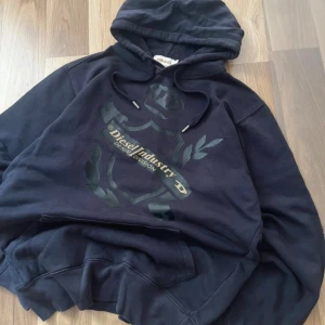 Svart hoodie från Diesel, storlek M (Passar som S) - Säljer en svart hoodie från Diesel med tryck på bröstet och snörning i huvan. Tröjan har en klassisk passform och är tillverkad i mjuk bomull. Perfekt för dig som gillar streetwear och vill ha något bekvämt och stilrent. Skulle säga den passar som en S. Kan sänka pris vid snabbt köp👍