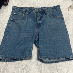 Blå denimshorts från 157 - Klassiska blå denimshorts från 157 med fem fickor, bälteshällor och dragkedja framtill. Raka ben och normal passform, perfekta för sommardagar. Tidlös design i bomull som funkar till allt.