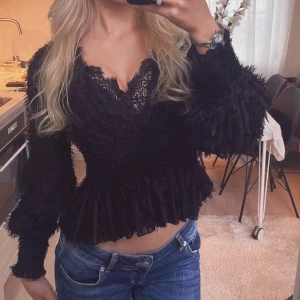 Svart blus med volang - Supersnygg svart blus med v-ringning. Blusen har långärmade puffiga ärmar och volang nertill. Materialet är strukturerat och ger en cool textur. 