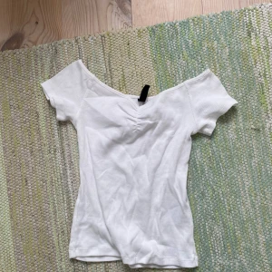Vit ribbad offshoulder topp H&M - Säljer en vit ribbad topp från H&M Divided med offshoulder-design och korta ärmar. Toppen har en snygg rynkning framtill vid bysten och är figurnära i modellen. Perfekt för dig som gillar en enkel men trendig look.
