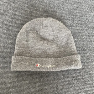 Grå mössa från Champion - Grå mössa från Champion med klassisk uppvikt kant och broderad logga framtill. Enkel och stilren design som passar perfekt till kalla dagar. Tillverkad i mjuk bomullsmix för skön komfort.