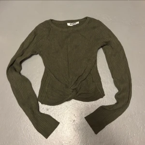 Olivgrön ribbad tröja från Misskiss (Italien)  - Snygg olivgrön tröja med lång ärm och twistad detalj framtill. Tröjan har rund halsringning och är figurnära i modellen. Superenkel att styla till jeans eller kjol.