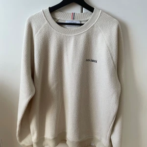Beige fleece-tröja från Les Deux - Säljer en beige fleece-tröja från Les Deux med broderad logga på bröstet. Tröjan har rund halsringning, långa ärmar och ribbade muddar. Perfekt för kyliga dagar och riktigt skön att ha på sig.