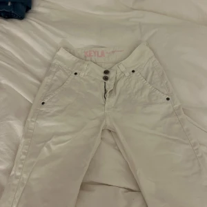 Vita byxor från Peak Performance - Snygga vita jeans  från Peak Performance med raka ben och coola detaljer som dubbla knappar framtill och fickor med lock och knapp bak. Byxorna har en klassisk passform och är vintage