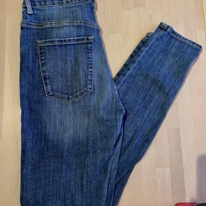 Blå Vera jeans från Lindex - Snygga blå jeans från Lindex Vera med klassisk femficksdesign och dragkedja. Jeansen har en rak passform och är tillverkade i bomull och polyester med lite stretch för extra komfort. Perfekta för dig som gillar en tidlös och enkel stil.