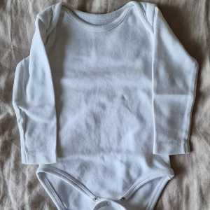 Vit långärmad body i ekologisk bomull - En basic vit långärmad body från Cubus i mjuk ekologisk bomull. Bodyn har rund halsringning och tryckknappar i grenen för enkel påklädning. Perfekt för lager-på-lager och superbekväm för de minsta.