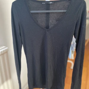 Svart ribbad långärmad tröja  - Svart långärmad tröja från lager 157 med v-ringning och ribbad struktur. Tröjan är figurnära och har en klassisk, enkel design som har ett tunt och mjukt material. 