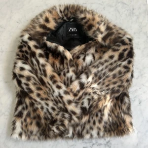Leopardmönstrad pälsjacka från Zara - Säljer en supercool pälsjacka från Zara i leopardmönster. Jackan är fluffig och har en snygg mix av bruna, svarta och beige toner. Perfekt statement-plagg med klassisk krage och helfodrad insida. Jackan är i kortare modell och har långa ärmar.