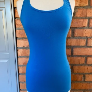 Blått linne från Eve strl S - Snygg blått linne från Eve i stretchig bomullsblandning. Modellen är figurnära med brottarrygg och rundad halsringning. Perfekt för en enkel och sportig look, lätt att matcha med jeans eller shorts.