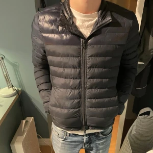 Mörkblå pufferjacka från J.Lindberg - Snygg mörkblå pufferjacka från J.Lindberg, passar i dom flesta väder så som vår vinter och höst. Väldigt fint skick då den vart för liten för mig fort. Pris ej hugget i sten.