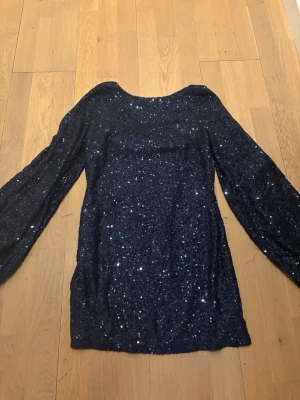 Glittrig mörkblå blus med paljetter - Glittrig mörkblå blus täckt av paljetter med rund halsringning och långa, puffiga ärmar. Blusen har en figurnära passform och ger en riktigt trendig look.