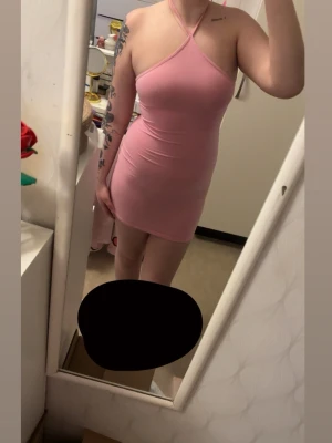 Rosa kort klänning med halterneck - Säljer en tight, kort rosa klänning med halterneck och smala axelband som korsas i nacken. Klänningen har en enkel, stilren design och är gjord i ett stretchigt material som sitter snyggt på kroppen. 