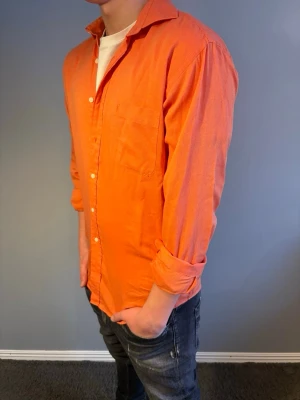 YSL skjorta - Säljer en snygg orange YSL skjorta i bomull klassisk krage och bröstficka. NYPRIS CA 18000kr. Skjortan har knappar framtill och långa ärmar som kan vikas upp för en mer avslappnad stil. Storlek L men passar M. Modellen är 184cm.