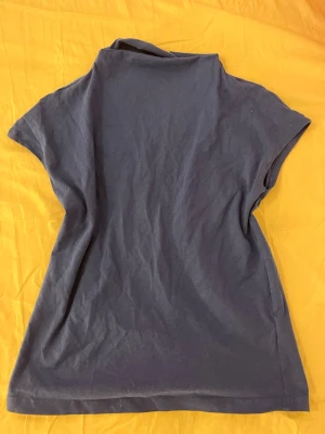 Mörkblå kortärmad topp - En enkel och stilren mörkblå topp med korta ärmar och rak passform. Toppen har en högre halsringning och är tillverkad i mjukt bomullsmaterial, perfekt för en avslappnad look.