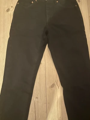 Svarta Levi's 501 jeans straight fit - Klassiska svarta Levi's 501 jeans med rak passform och femficksdesign. Jeansen har knappgylf och är tillverkade i slitstarkt bomullsjeans. Perfekta för dig som gillar en tidlös och clean look.