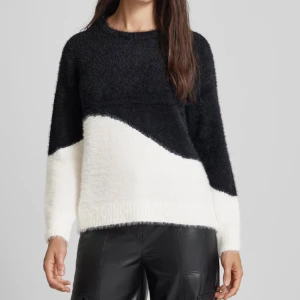 Svartvit stickad tröja från Vila - Mysig stickad tröja från Vila i svart och vitt med cool diagonal färgblockdesign. Tröjan har rund halsringning, långa ärmar och är gjord i ett fluffigt, mjukt material som känns riktigt skönt mot huden. Perfekt för dig som gillar en avslappnad men trendig stil.