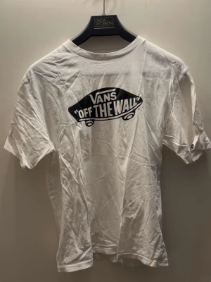 Vans "Off The Wall" Logo T-Shirt - White - Kids XL - Classic white t-shirt from Vans featuring the iconic "Off The Wall" skateboard logo on the front.  Condition: Sparingly used and well-maintained.  Size: XL in Youth/Kids size.  Color: White with black graphic.  Material: 100% Cotton, soft and comfortable for everyday wear.