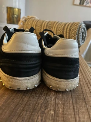 Valentino svartvita Rockrunner sneakers - Säljer ett par svarta och vita Valentino Rockrunner sneakers med coola nitar på sulan. Skorna har snörning, rund tå och är tillverkade i mocka och skinn. Perfekta för dig som gillar en edgy och stilren look.