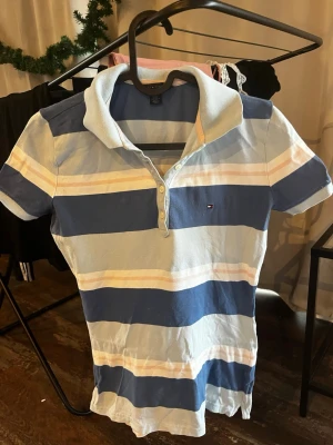 Randig pikétröja Tommy Hilfiger XS - Snygg randig pikétröja från Tommy Hilfiger i ljusblått, mörkblått, vitt och ljusrosa. Klassisk krage, korta ärmar och knappar framtill. 
