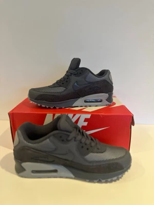 Nike Air Max 90 mörkgrå sneakers WMNS - Snygga mörkgrå Nike Air Max 90 sneakers med klassisk siluett. Skorna har mesh- och syntetpaneler, synlig Air-enhet i sulan och rund tå. Perfekta för dig som gillar stilrena och sportiga sneakers. 