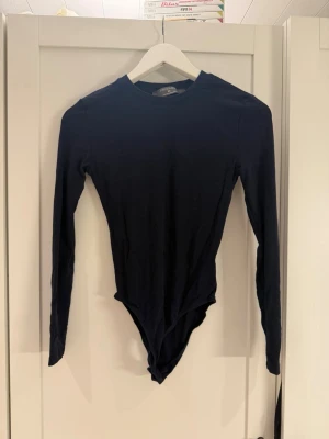 Svart långärmad body från Primark - En enkel och stilren svart body från Primark i storlek XS. Bodyn har långa ärmar, rund halsringning och är tillverkad i ett mjukt stretchigt material som sitter snyggt på kroppen. Perfekt att matcha med jeans eller kjol.