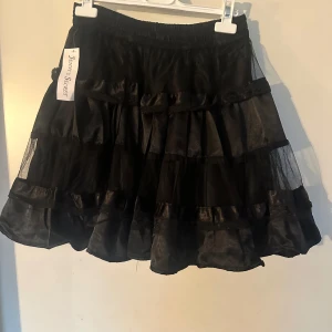 Kjol med resår i midjan onesize - Supersöt svart kjol med flera lager volanger och transparenta partier. Kjolen har resår i midjan och en fluffig, lekfull look som passar perfekt till en trendig outfit. Helt ny. Resår i midjan. Helt ny.