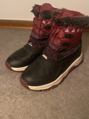 vinterstövlar med fuskpäls - Säljer vinterstövlar med snörning och fuskpäls runt skaftet. Stövlarna har en robust sula och quiltad ovandel, perfekta för kalla dagar. Snygg design med vita detaljer och mönstrad kant upptill. Varma och mjuka