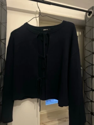 Svart croppad tröja med knytning - Trendig svart croppad tröja från GINATRICOT med öppen front och tre knytband. Tröjan har långa ärmar och rund halsringning. Perfekt för lager på lager och en cool vardagslook.