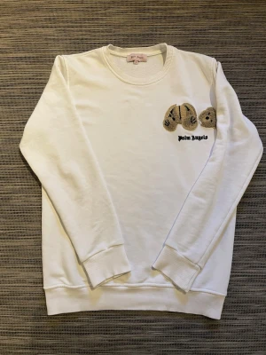 Vit sweatshirt från Palm Angels S - Säljer en vit sweatshirt från Palm Angels i storlek S. Tröjan har ett broderat nallemotiv på bröstet och klassisk rund hals. Tillverkad i mjuk bomull med ribbade muddar vid ärmslut och nederkant. Perfekt för dig som gillar streetwear och snygga detaljer. Om ni har några frågor så är det bara att höra av er!😊