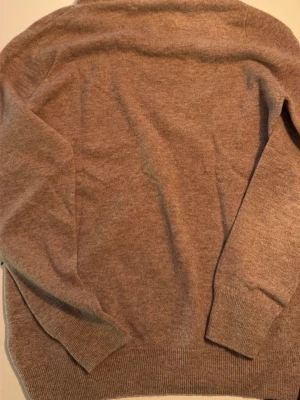 Beige stickad hoodie med dragsko - Mysig beige stickad hoodie med huva och dragsko. Tröjan har långa ärmar, ribbade muddar och nederkant. Perfekt för dig som gillar en avslappnad och stilren look. Materialet känns mjukt och skönt mot huden.