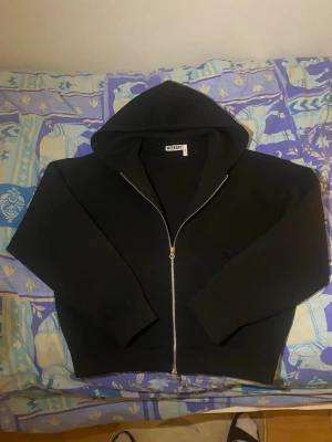 Svart hoodie med dragkedja från Weekday - Säljer en svart hoodie från Weekday i storlek S. Hoodien har dragkedja framtill, stor huva och ribbade muddar vid ärmslut och nederkant. Perfekt för en avslappnad och stilren look. Materialet känns mjukt och bekvämt.