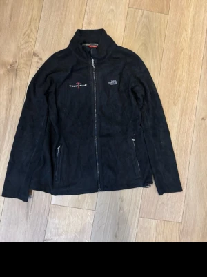 Svart fleecejacka från The North Face - Svart fleecejacka från The North Face med broderad logga på bröstet och dragkedja framtill. Jackan har hög krage, två fickor med dragkedja och diskret Telluride-brodyr. Perfekt för lager-på-lager och outdoor.