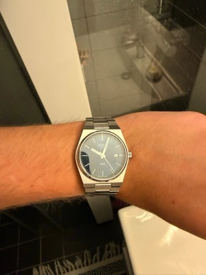 Tissot PRX klocka med blå urtavla - Snygg Tissot PRX klocka i rostfritt stål med blå urtavla och datumvisning. Klockan har en stilren, modern design med länkarmband och silverfärgade detaljer. Perfekt accessoar för dig som gillar klassisk men trendig stil.